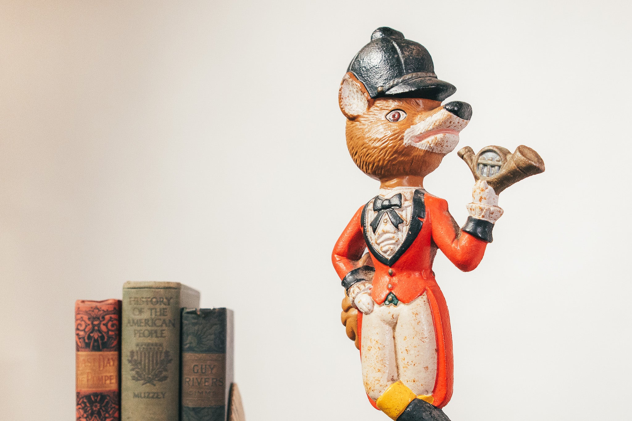 Fox figurine in a suit holding a clock with books in the background