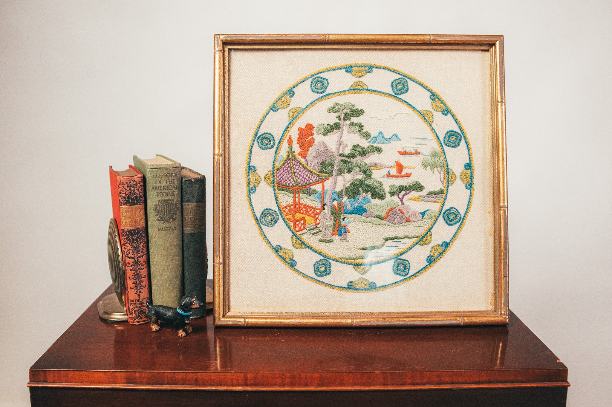 Framed decorative plate with a colorful design on a wooden surface with books.