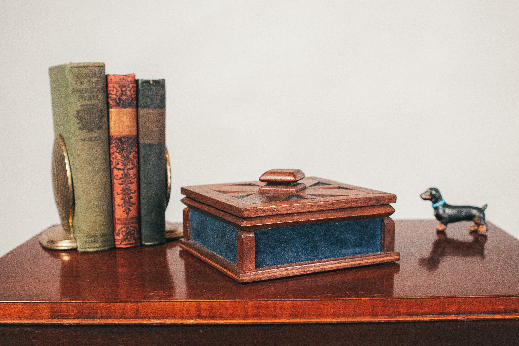 Wooden box with a blue interior on a wooden surface with books and a small dog figurine.