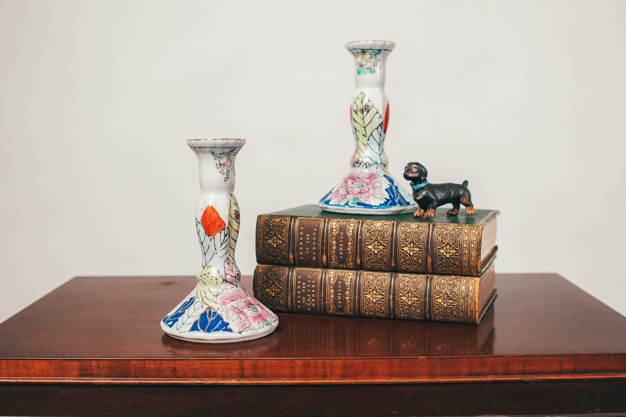 Decorative items including a small statue, books, and two vases on a wooden surface with a plain background.