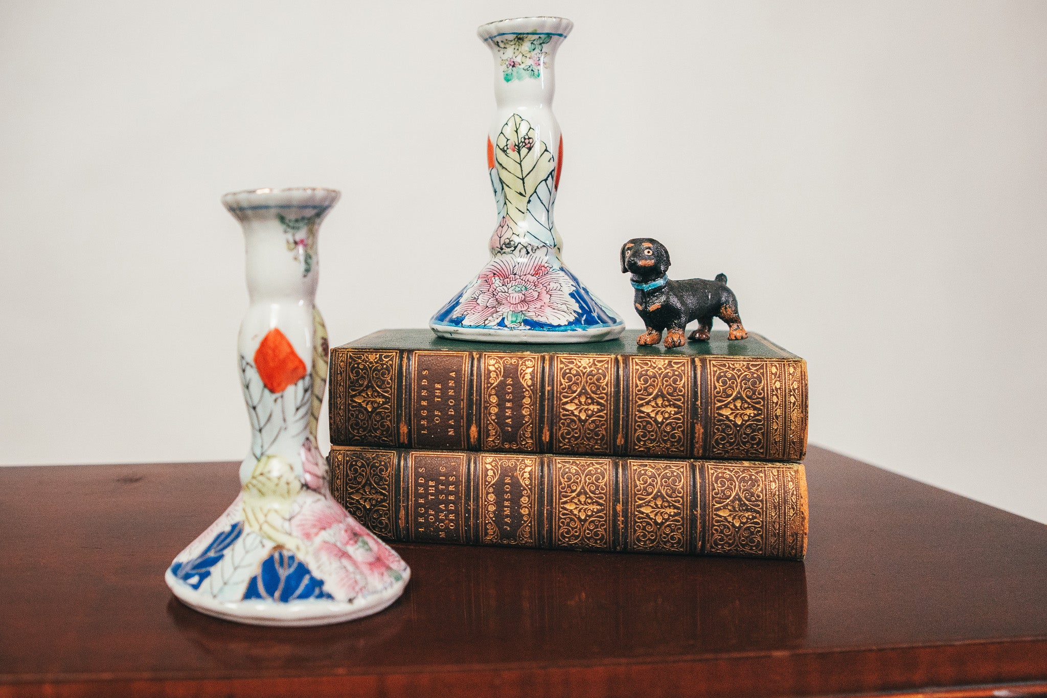 Two decorative vases and a small dog figurine on ornate books on a wooden surface.