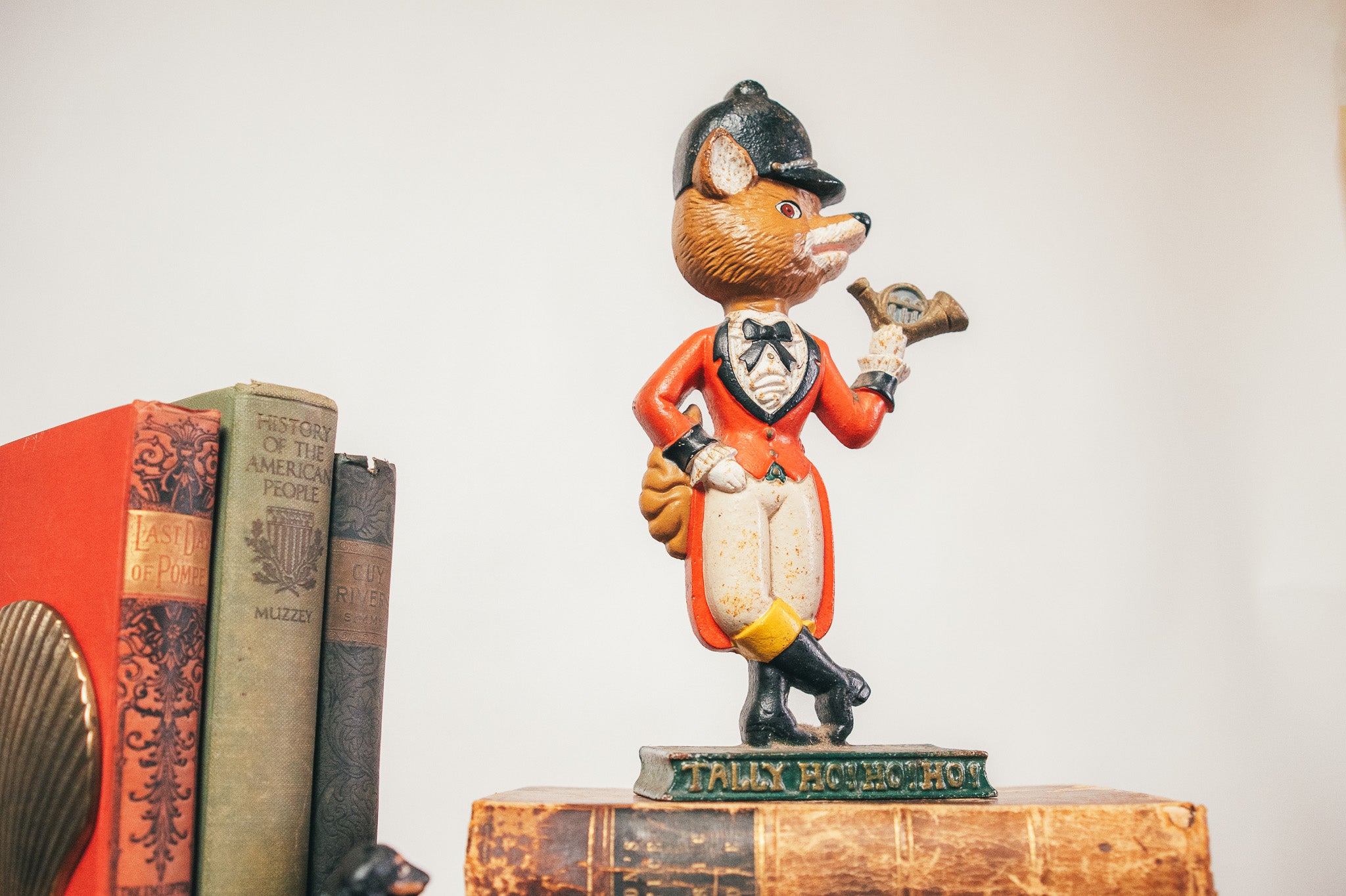 Vintage-style figurine of a fox in a suit on top of old books with a plain background