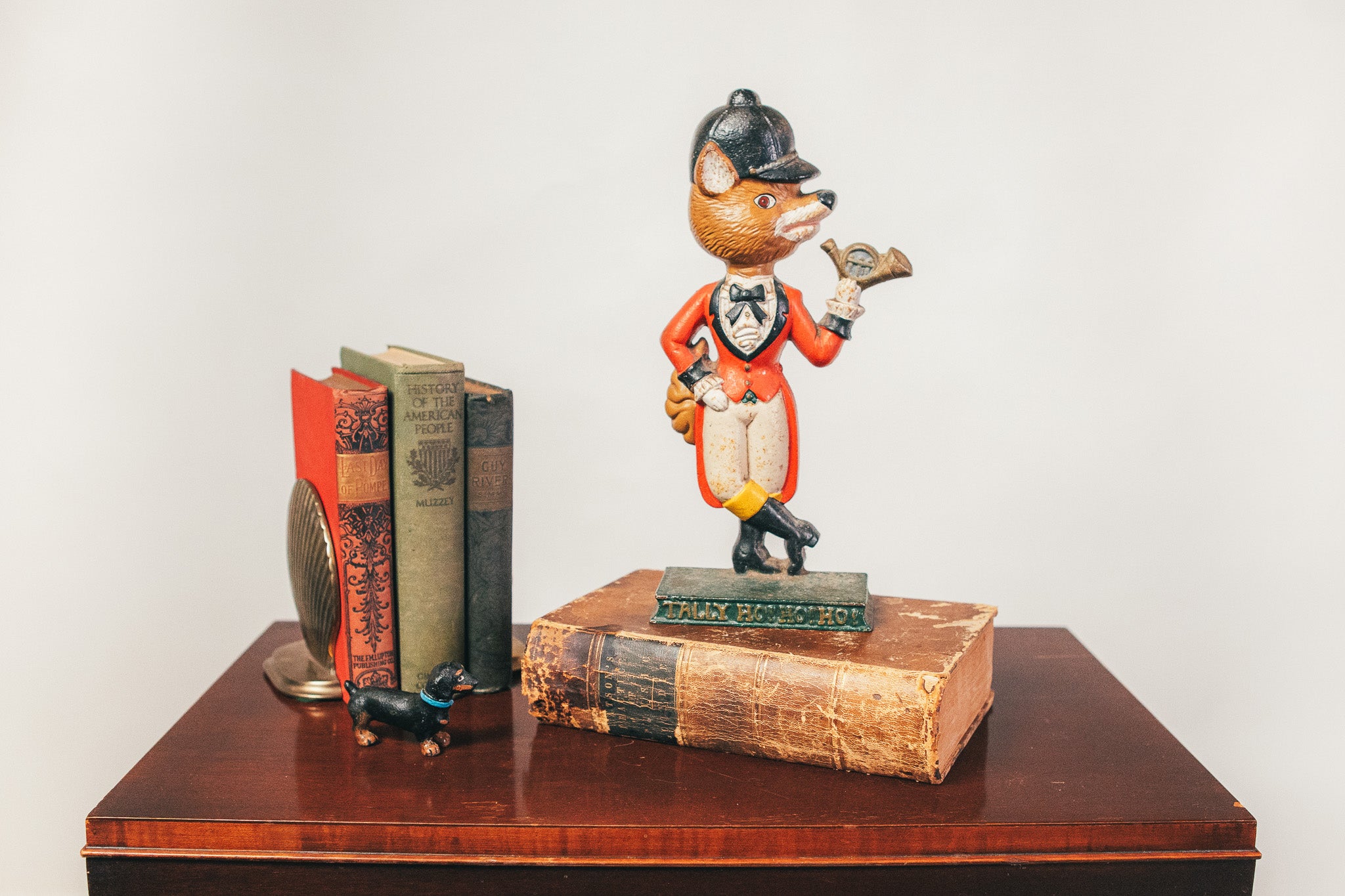 Vintage fox figurine with a hat on top of books on a wooden surface.