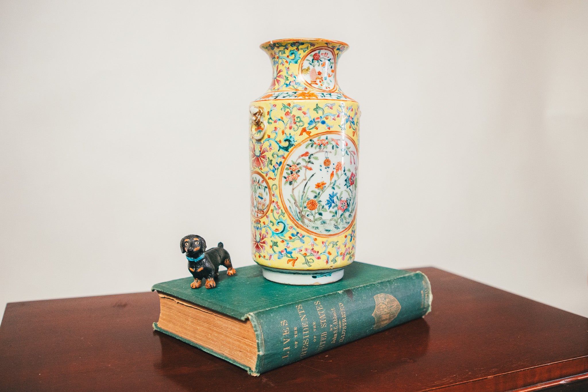 Colorful ceramic vase on a book with a small figurine on a wooden surface