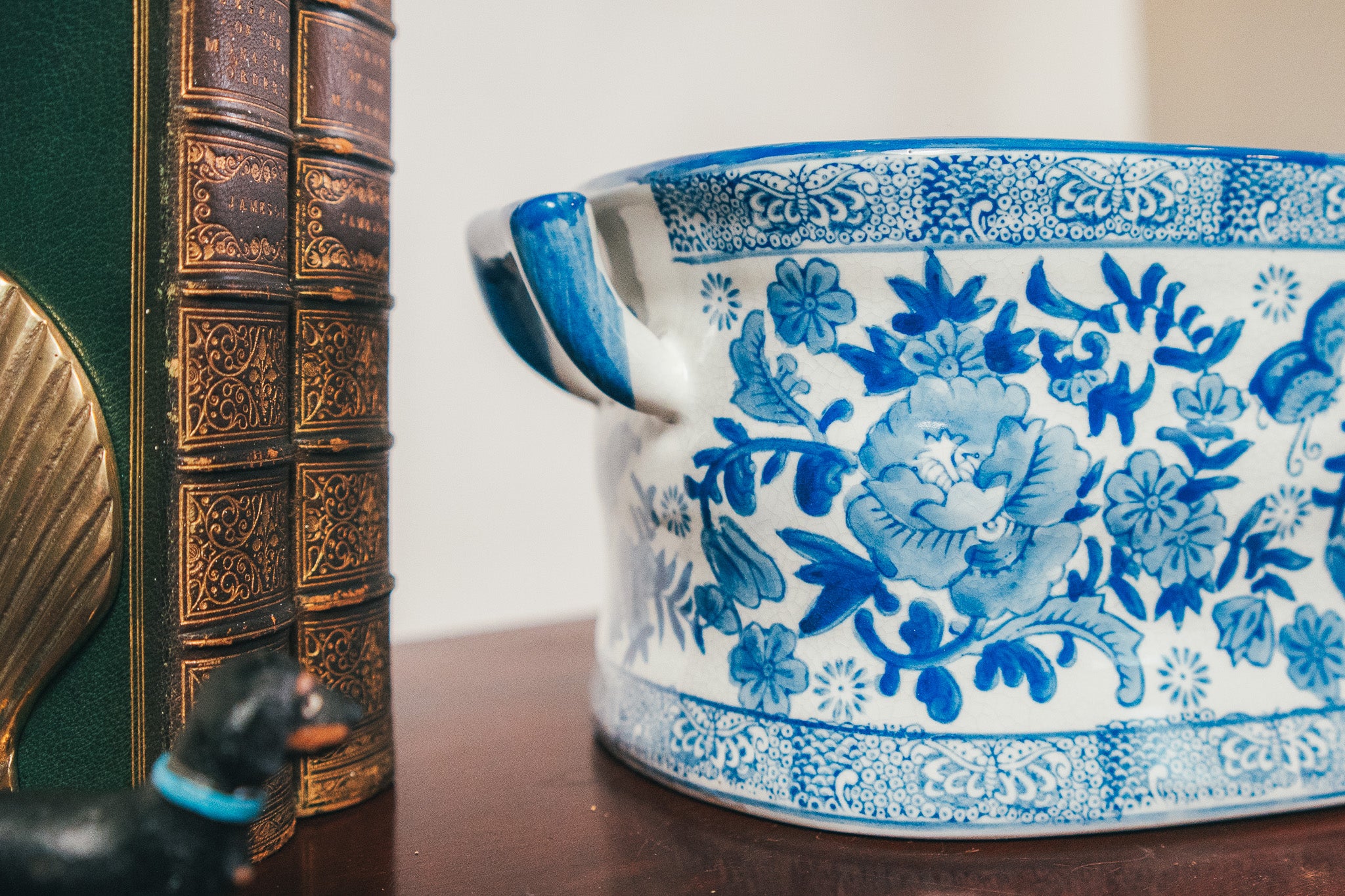 Blue and white ceramic pot with floral patterns next to a decorative book on a wooden surface.