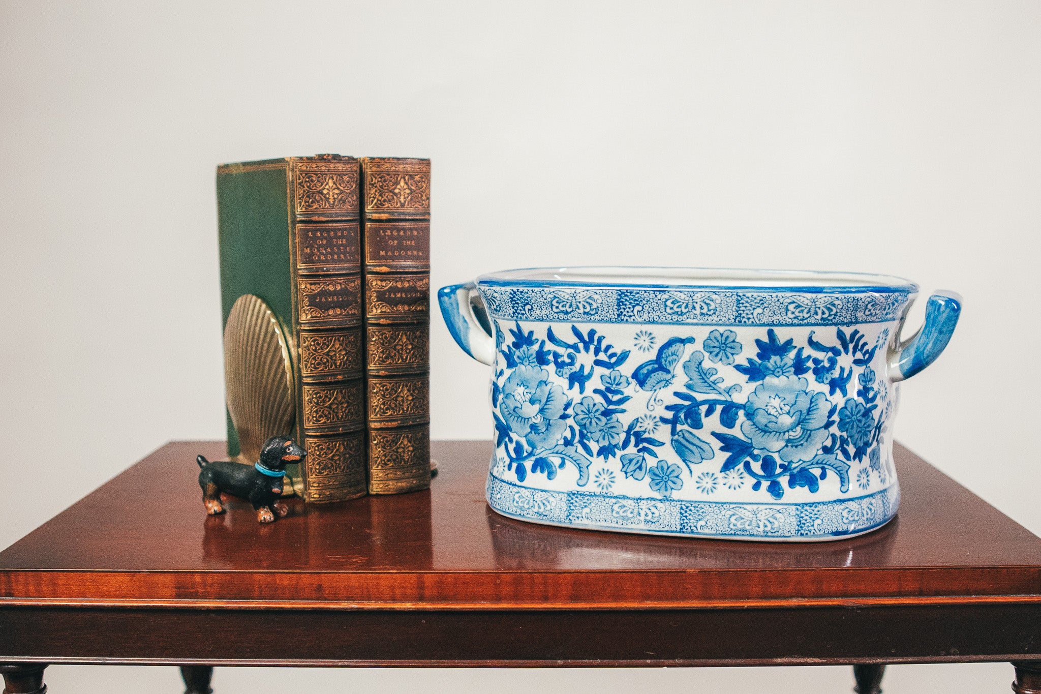 Decorative blue and white ceramic pot on a wooden surface with a book and small figurine.