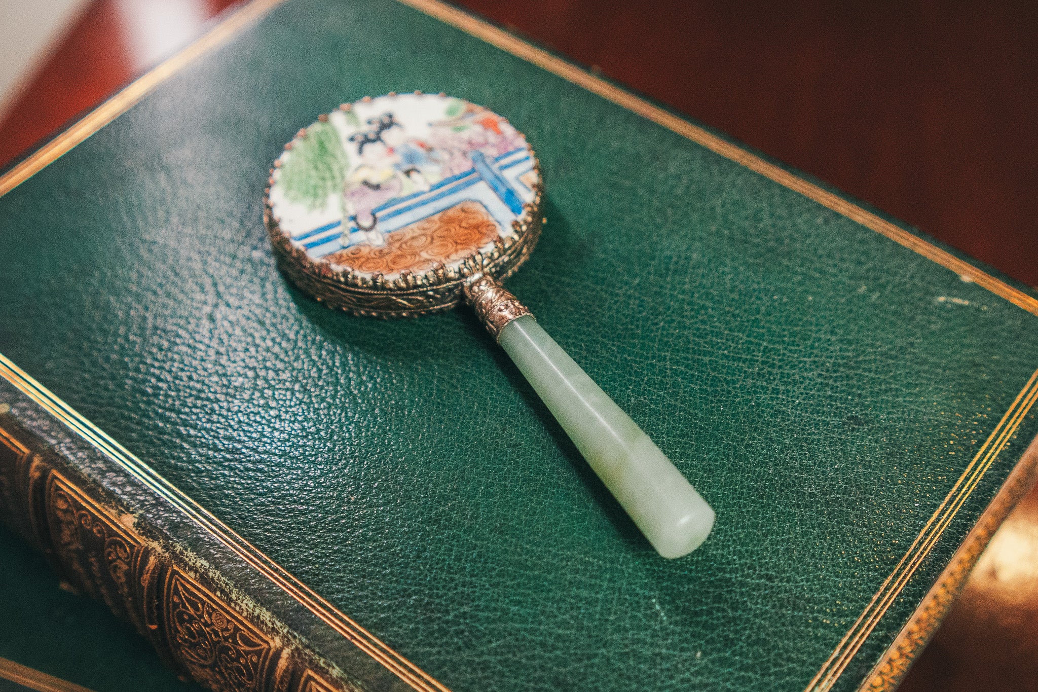 Decorative hand mirror with a jade handle on a green leather book