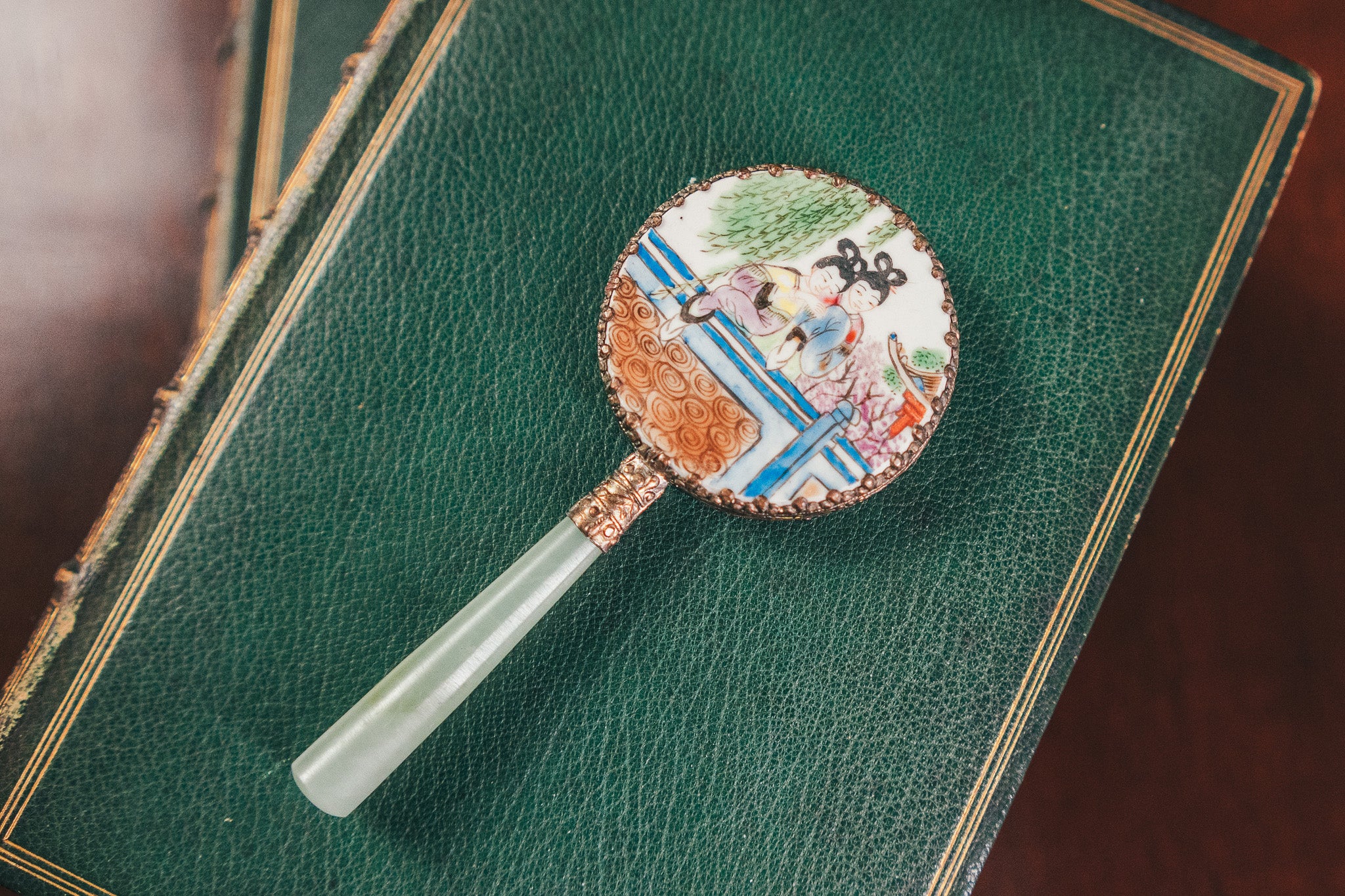 Decorative hand fan with intricate design on a green leather surface