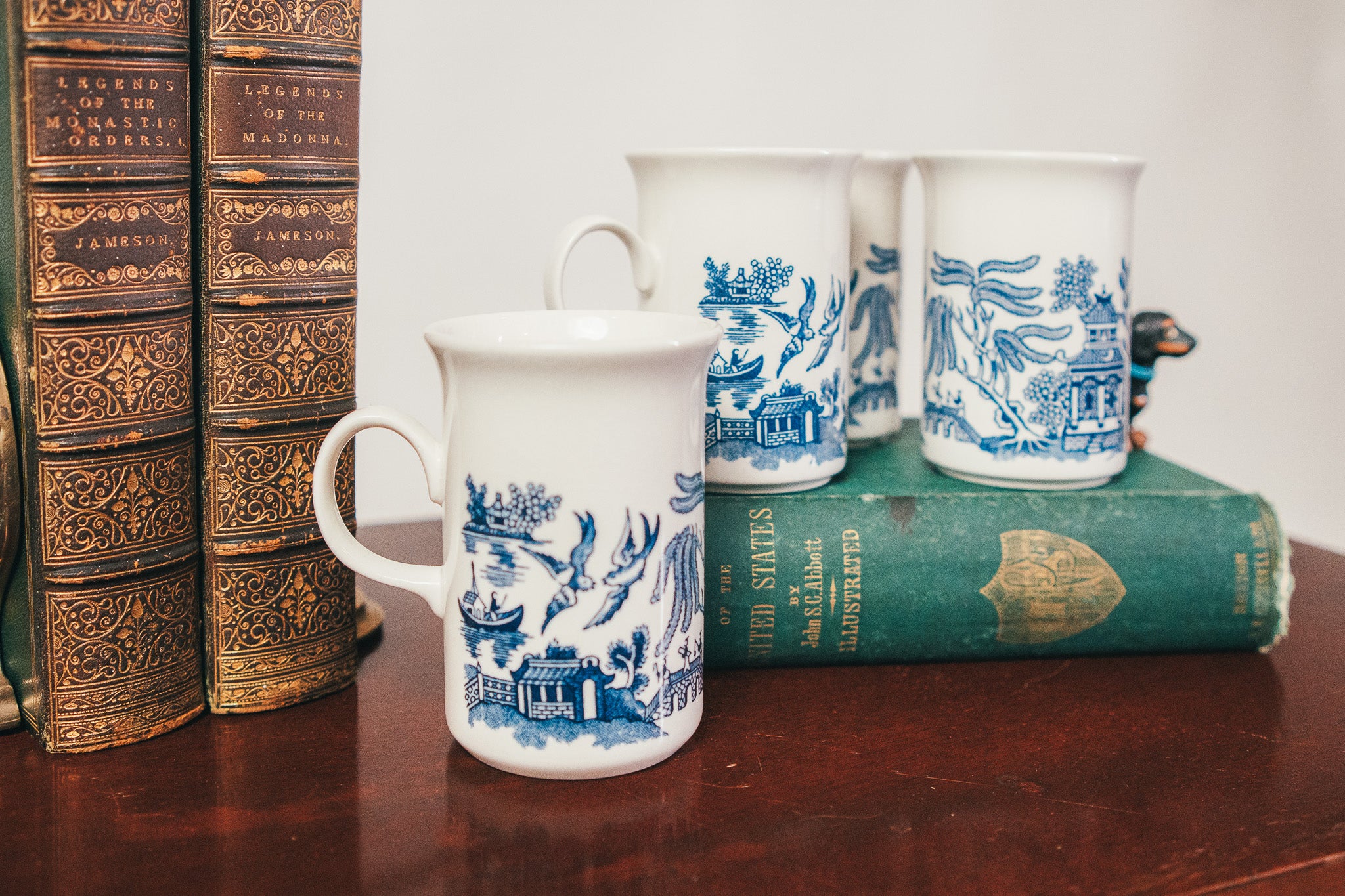 White mugs with blue patterns on a wooden surface with books