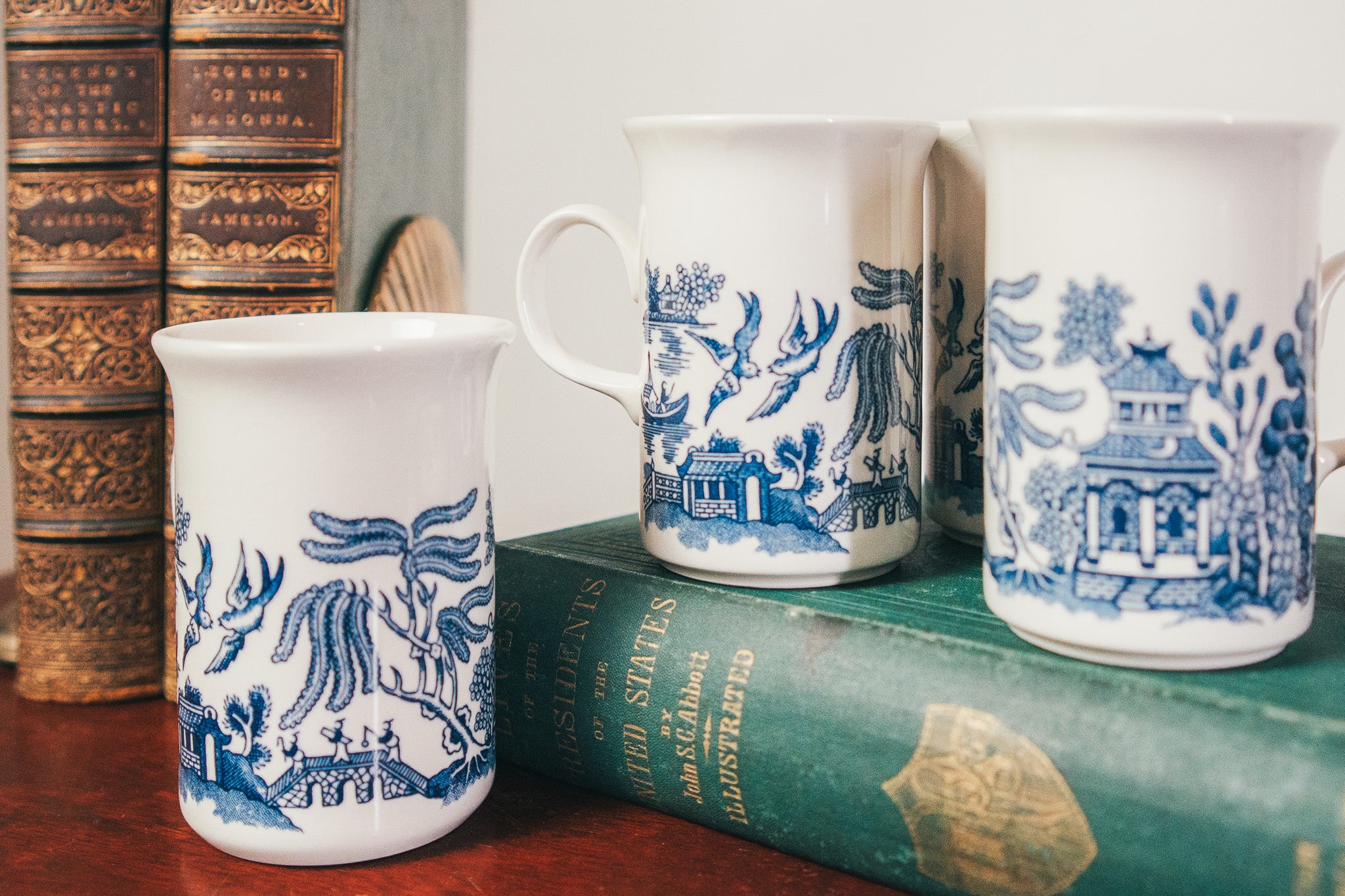 Three white mugs with blue floral patterns on a stack of books.