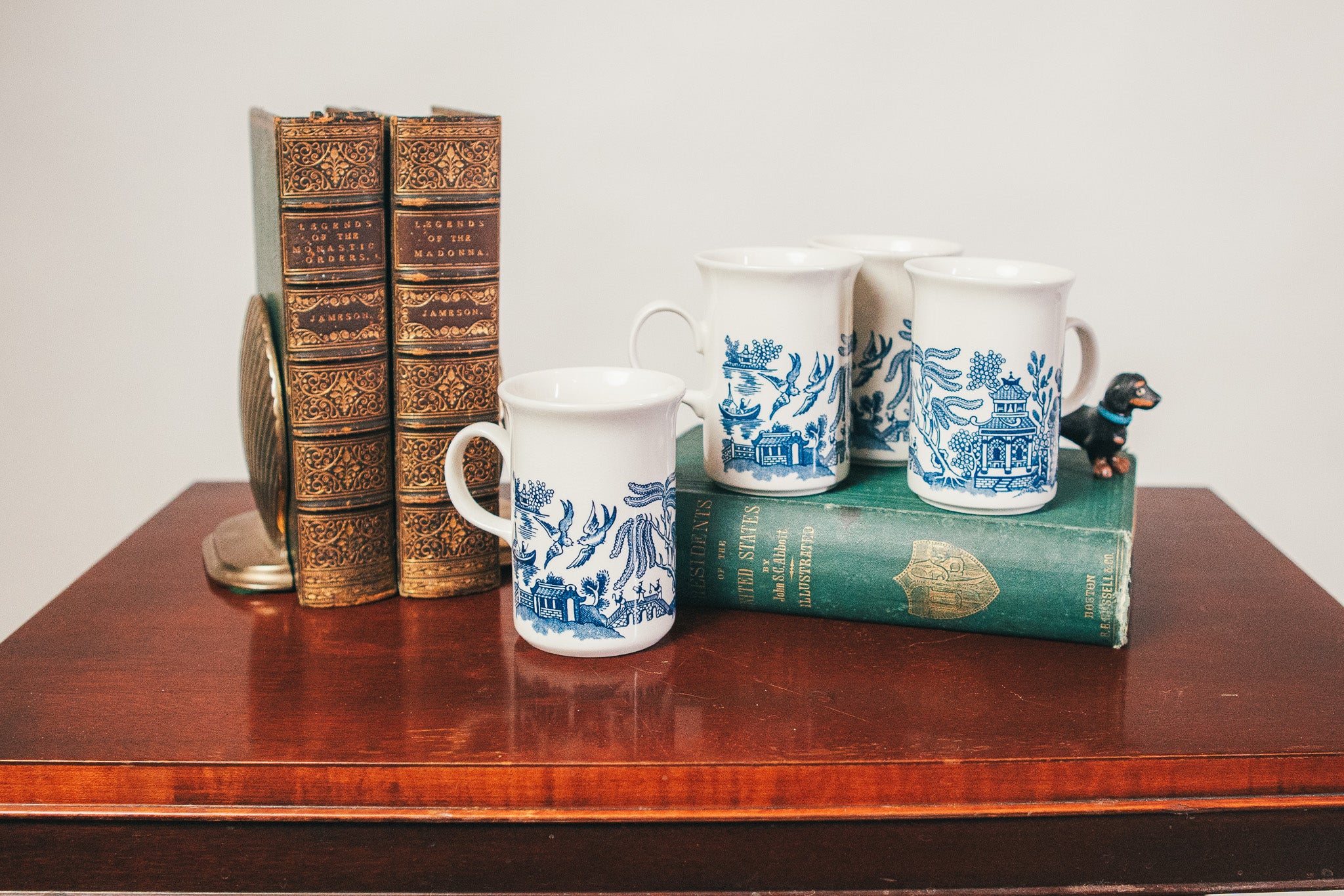 Three mugs with blue and white patterns on a wooden surface with books and a small figurine.