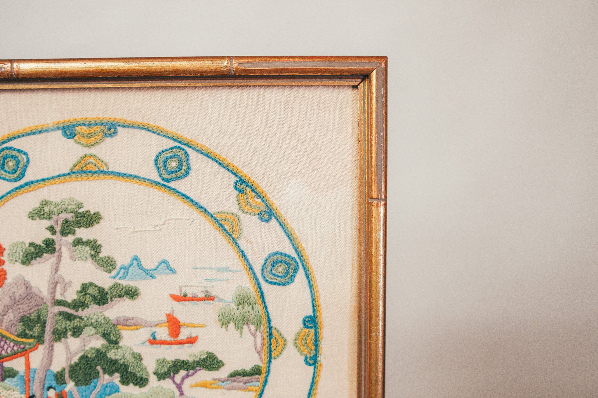 Framed embroidered artwork depicting a scenic landscape with mountains and boats.