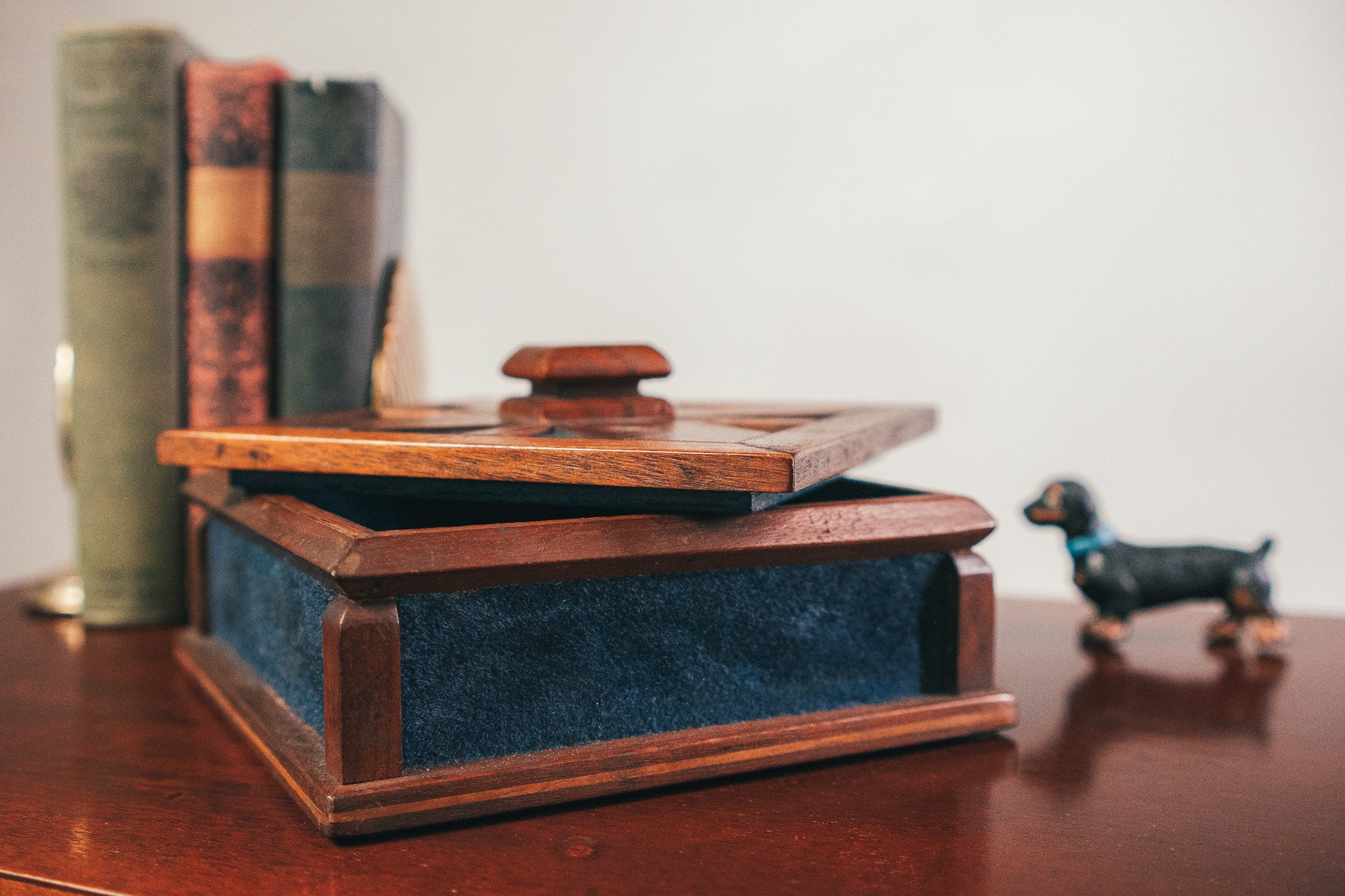 Wooden jewelry box with blue interior on a wooden surface, with books and a small dog figurine in the background.