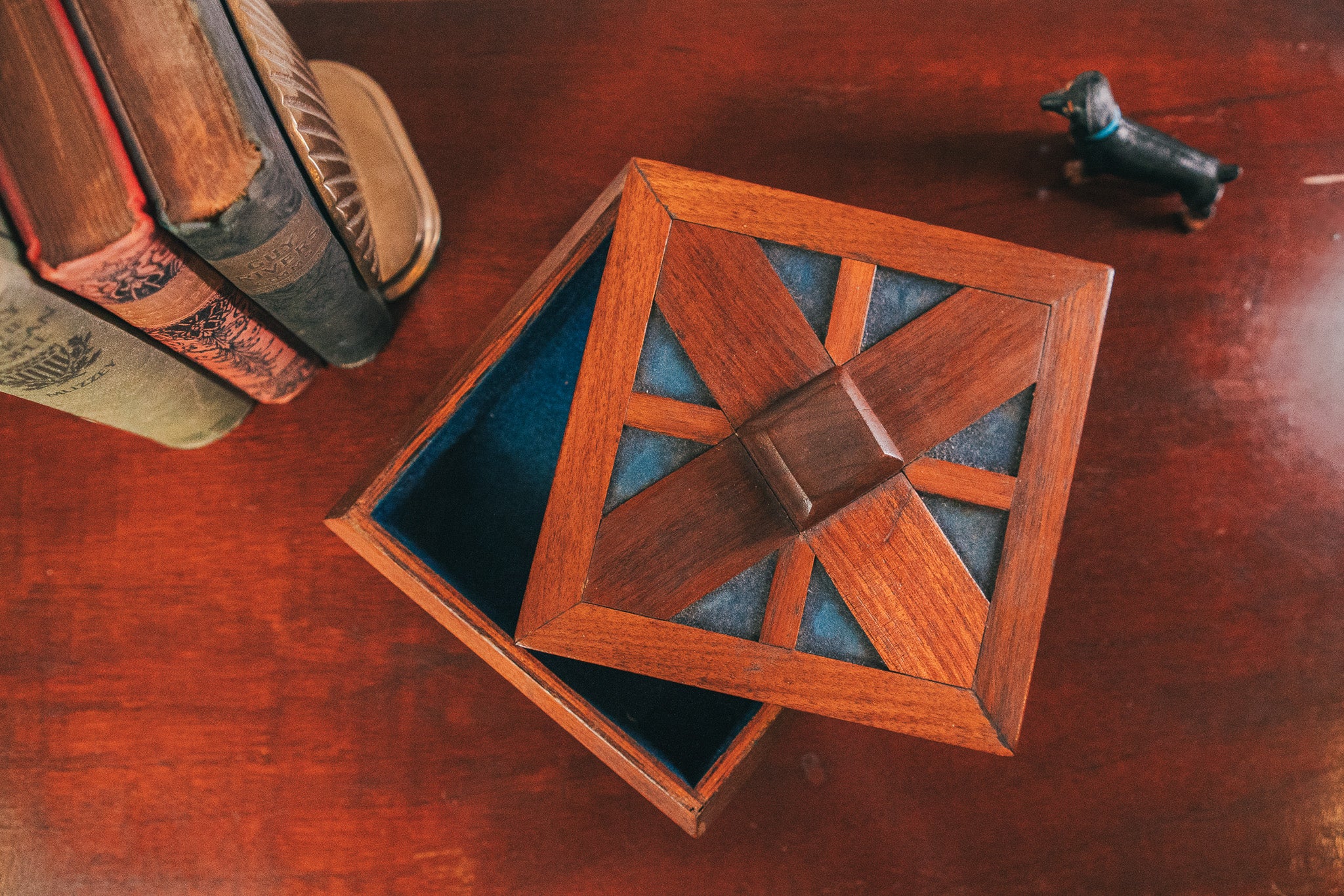 Wooden puzzle box on a wooden surface with books and a small figurine in the background