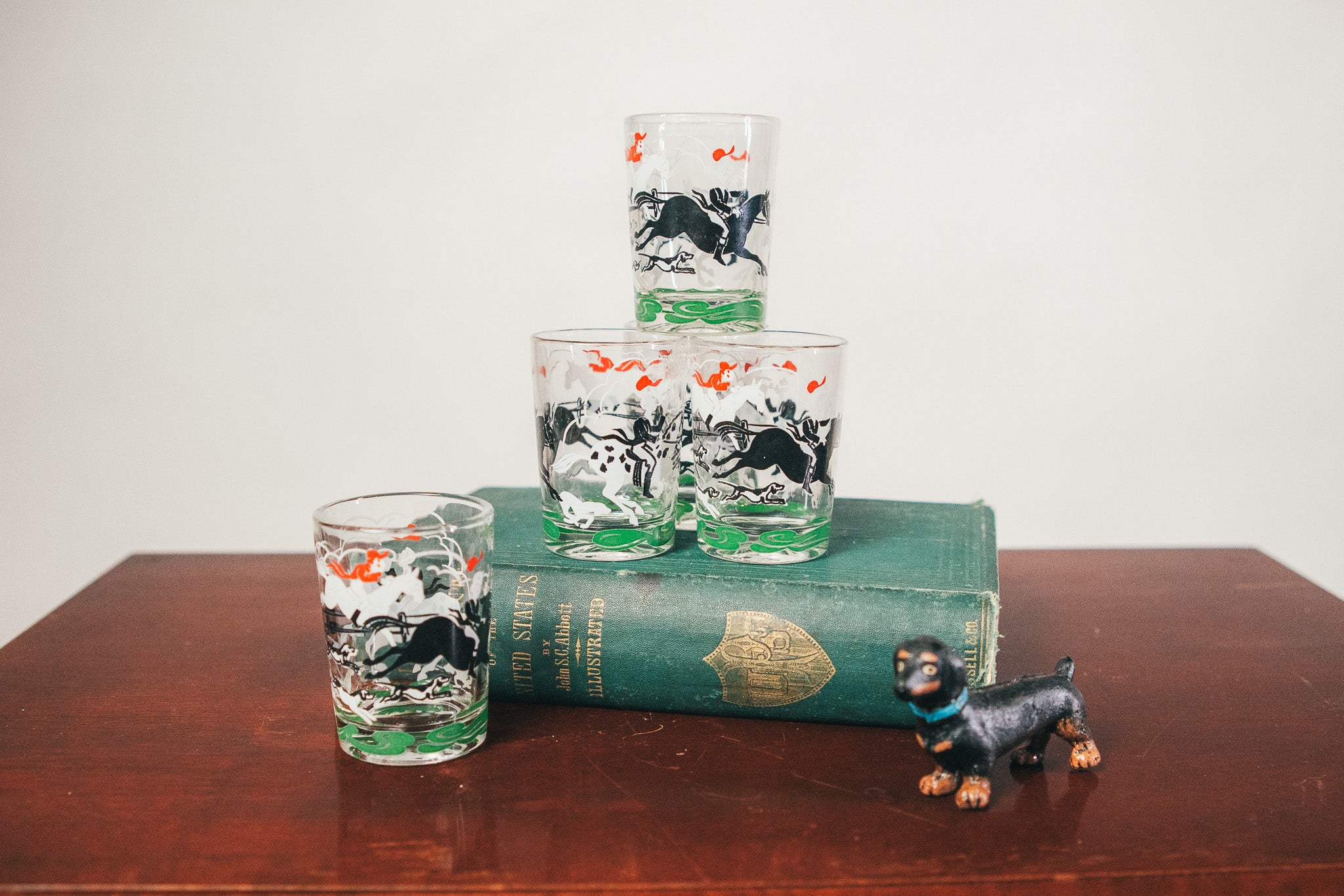 Set of four glass tumblers with horse design on a wooden surface with a book underneath.
