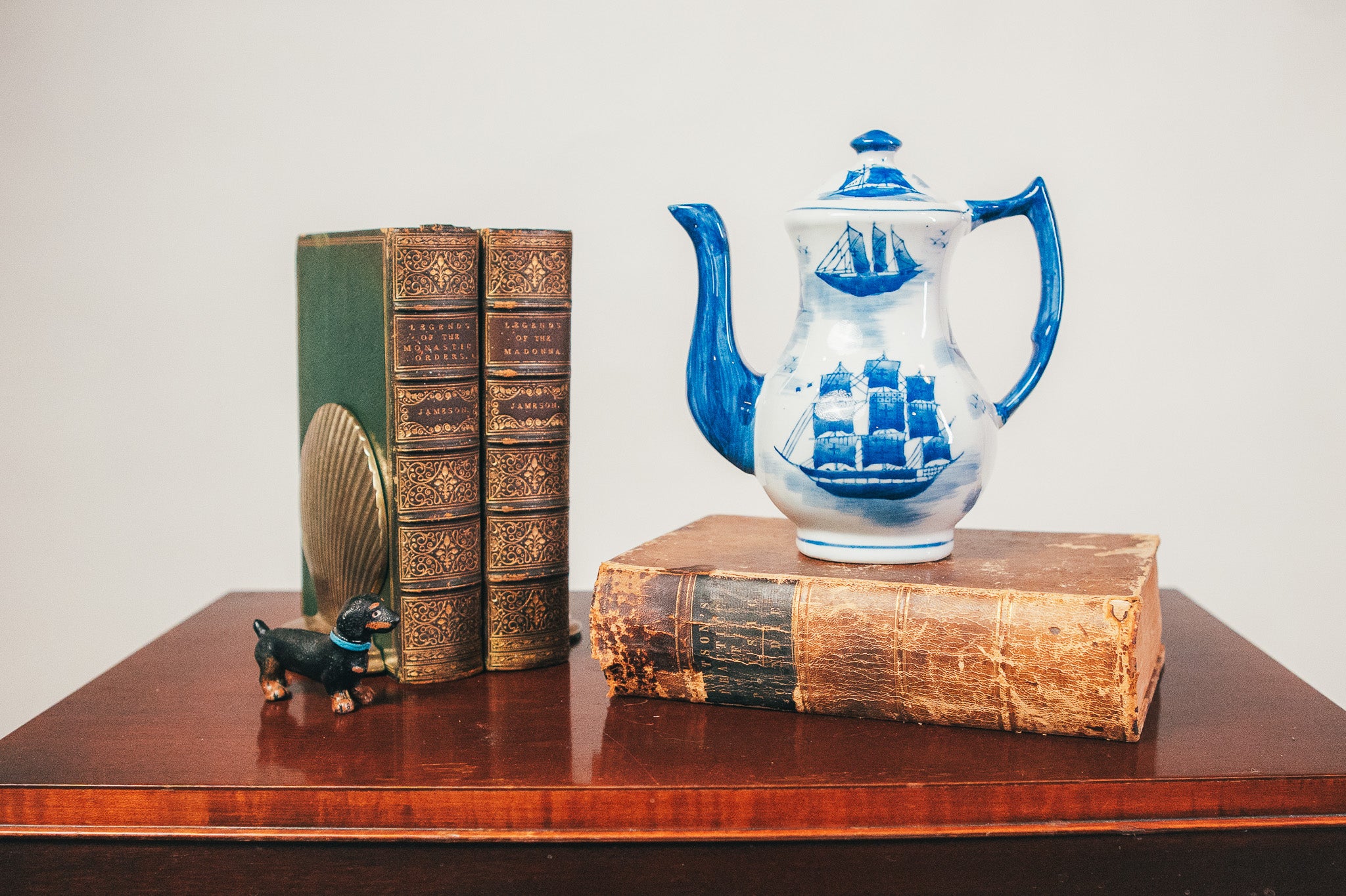 Blue and white ceramic teapot on a stack of vintage books with a small figurine and decorative item.