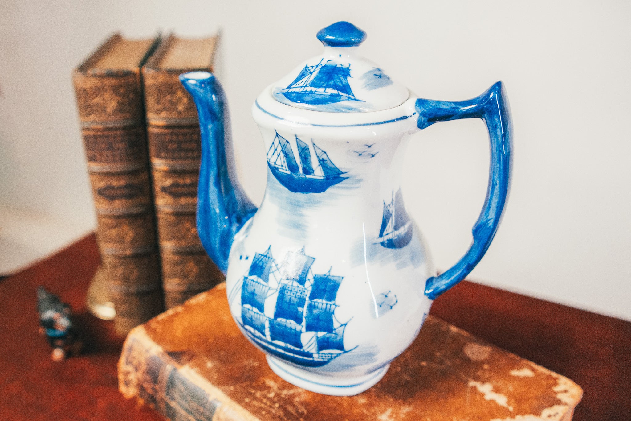 White teapot with blue ship designs on a wooden surface with books in the background
