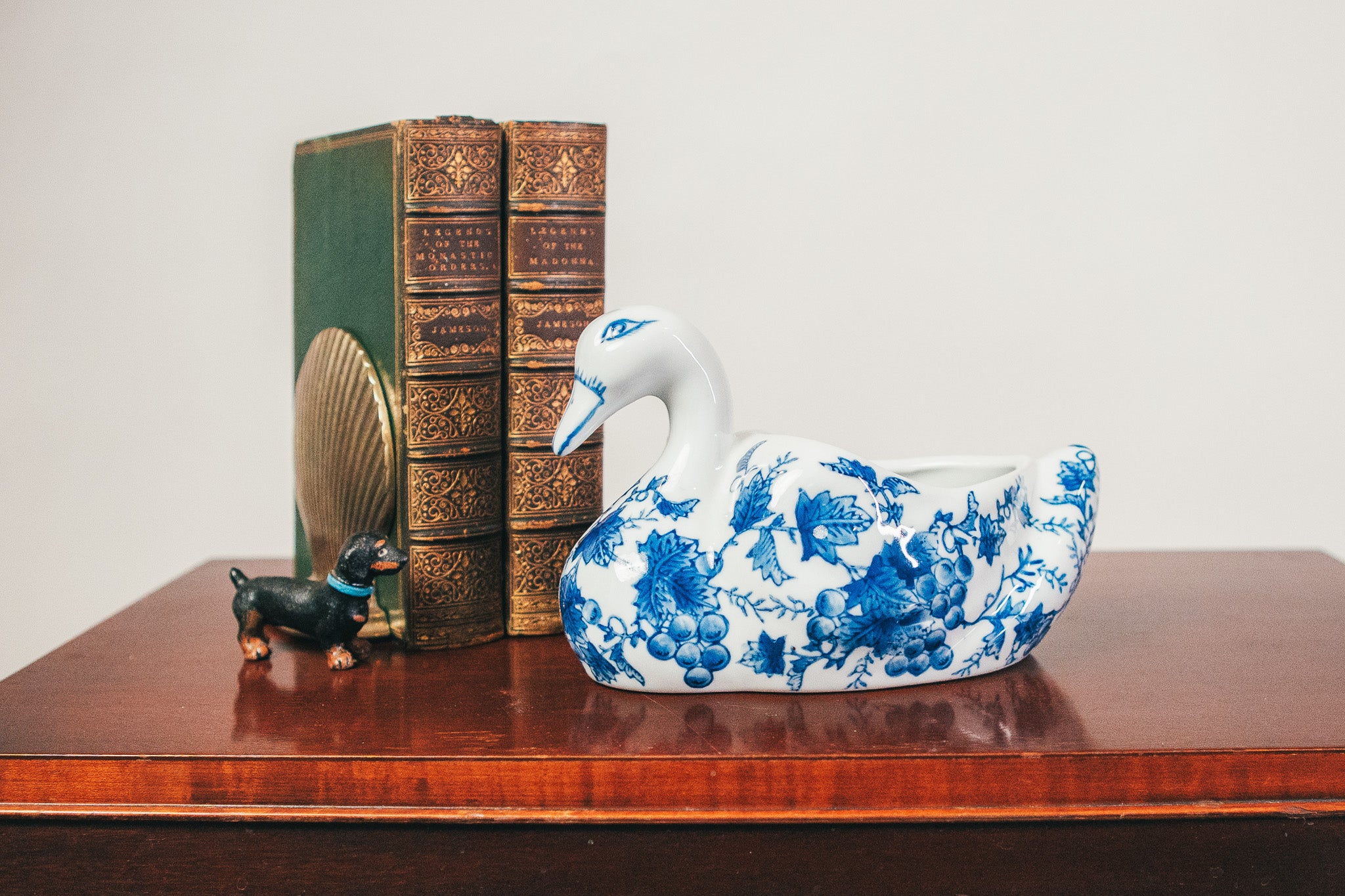 Decorative swan figurine with blue floral patterns on a wooden surface with books and a small dog figurine.