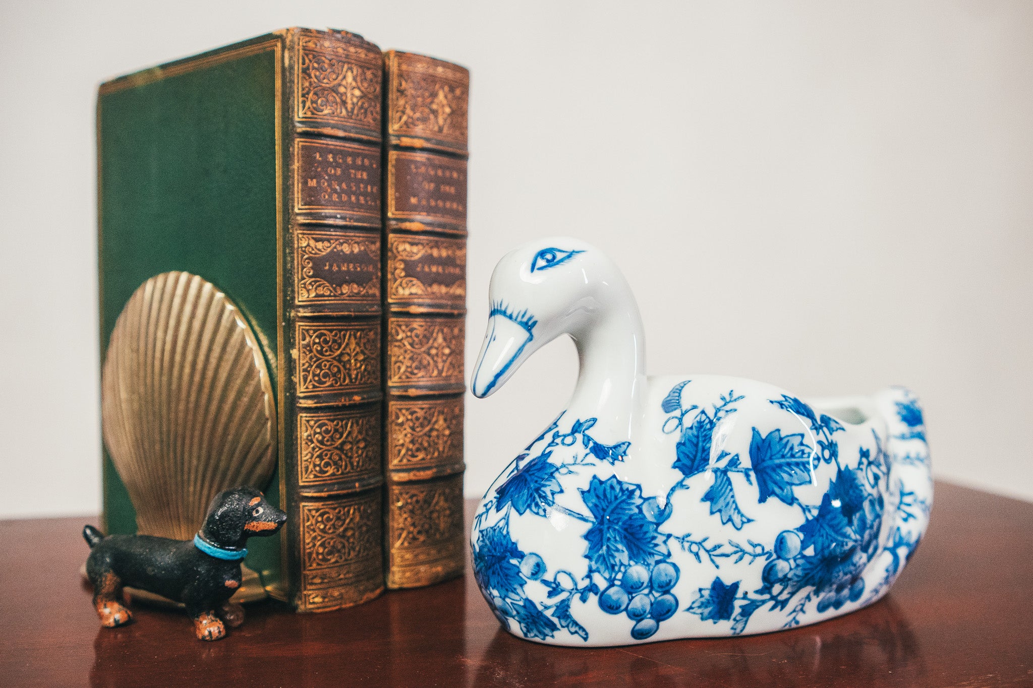 Decorative swan figurine with blue floral patterns next to a vintage book and small dog figurine on a wooden surface.