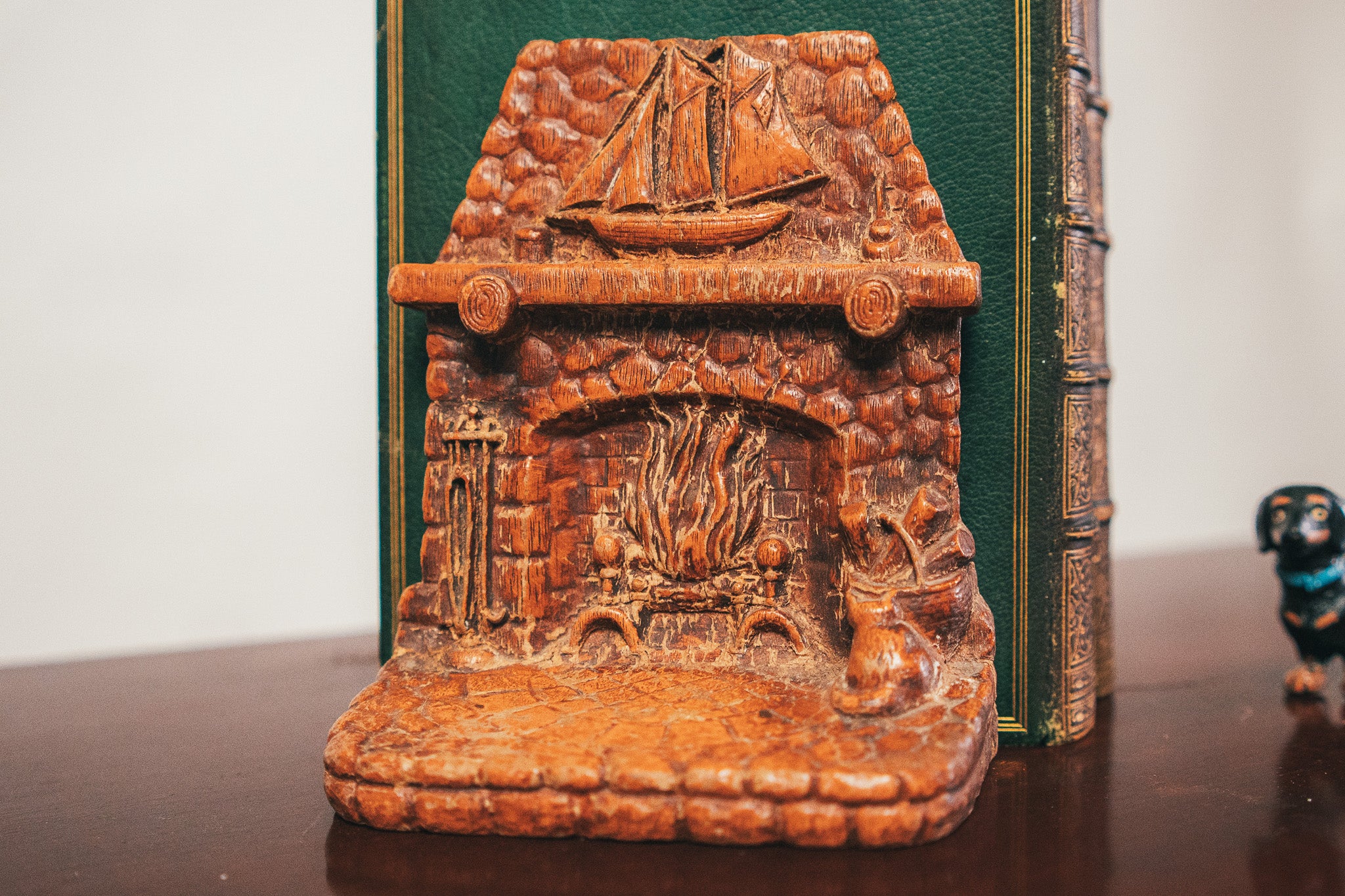 Carved wooden bookend with a ship and fireplace design on a green book.