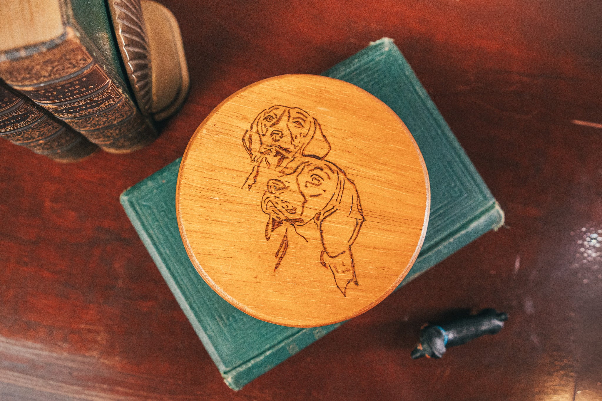 Wooden coaster with engraved design on top of a book on a wooden surface